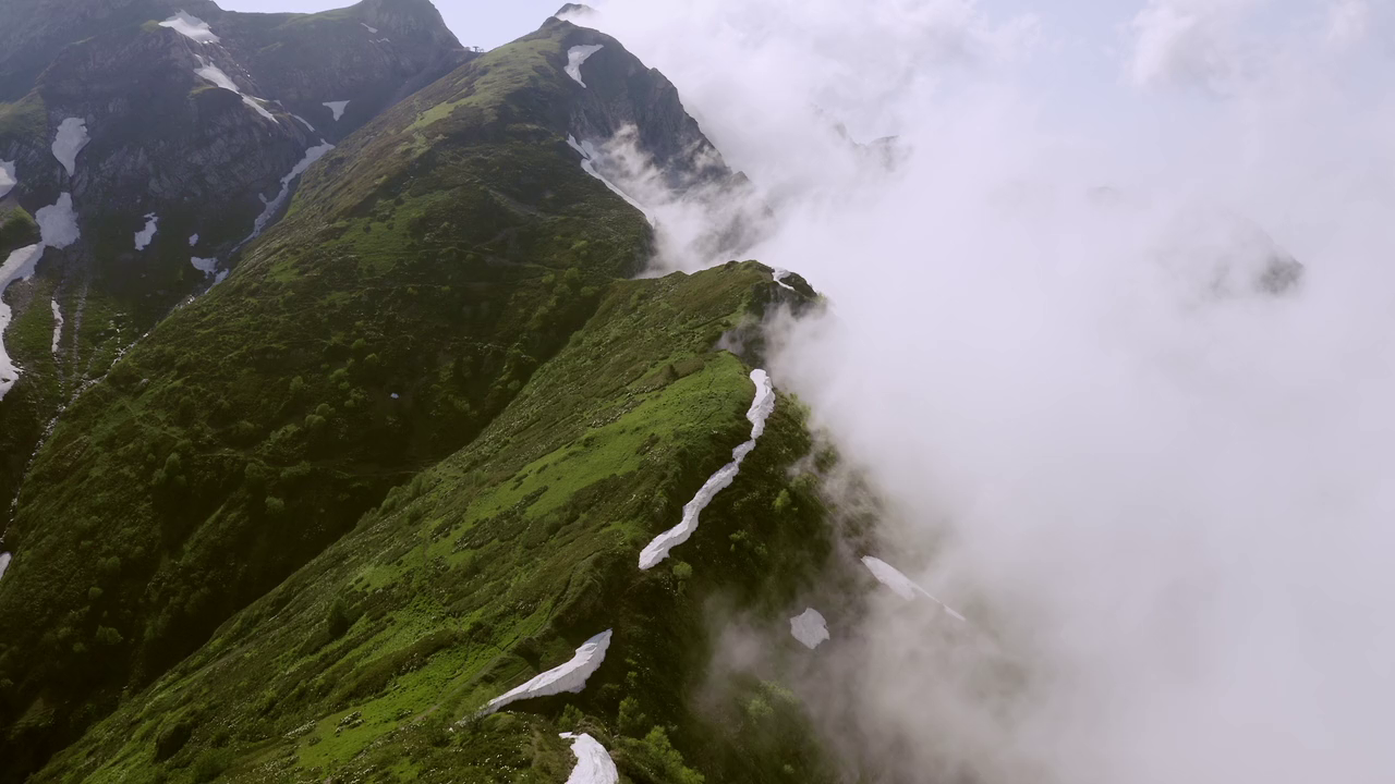 Ariel drone view of mountainous landscape with rolling clouds flowing over peak